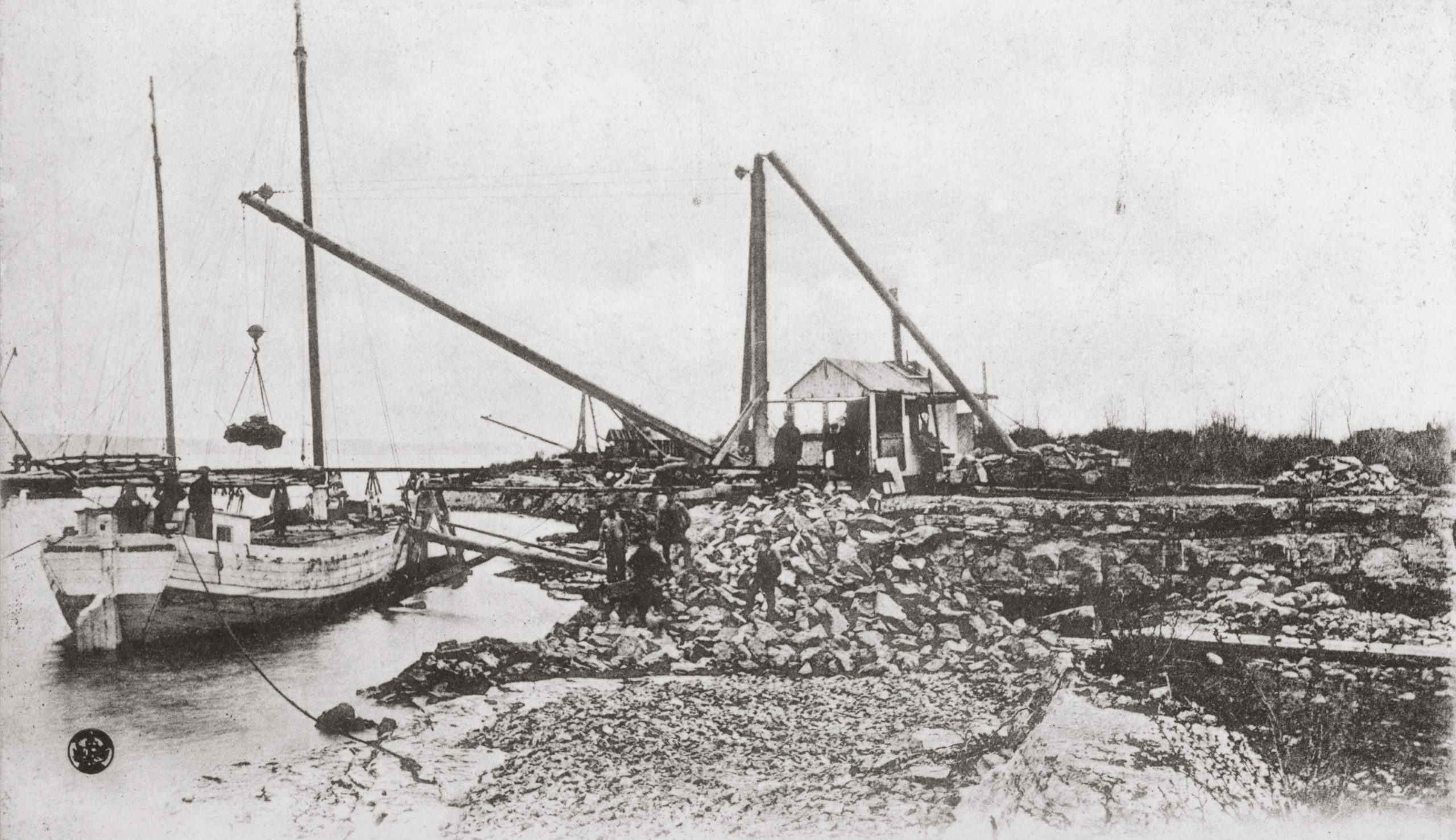 Black and white photo of a quarry on the water's edge and a boat being loaded.