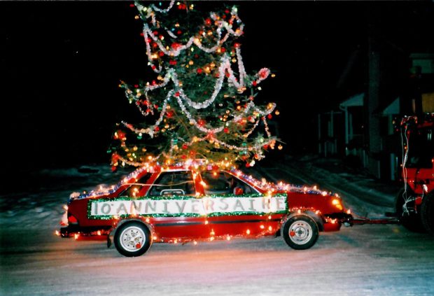 Red car decorated with lights and a Christmas tree on the roof. It says ‘10th Anniversary’.