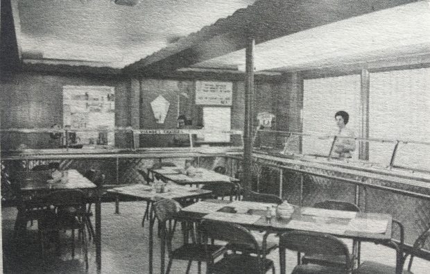 Black and white photo of the interior of the cafeteria at the Petite vache restaurant. Two ladies are behind the counter.