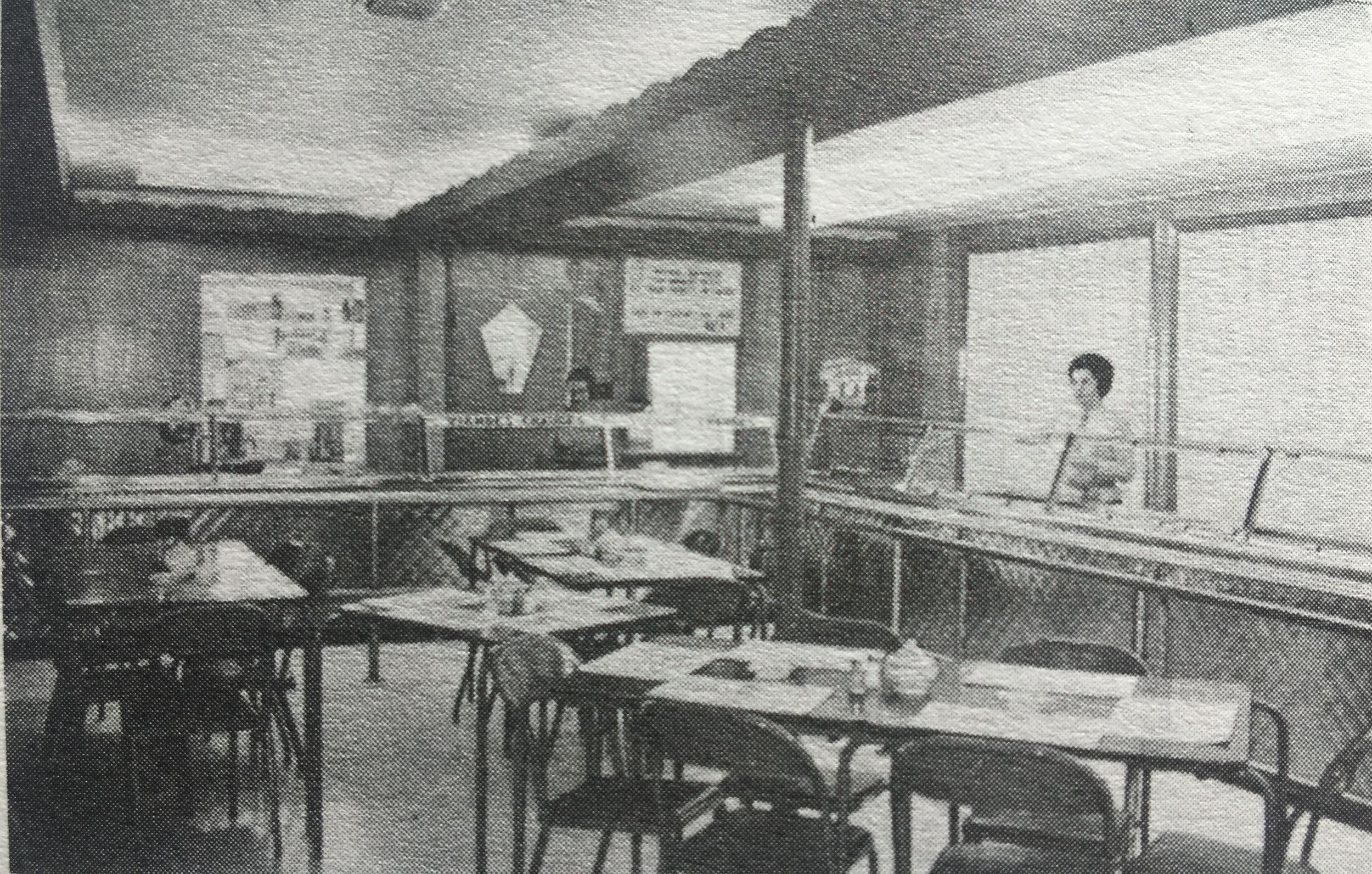 Black and white photo of the interior of the cafeteria at the Petite vache restaurant. Two ladies are behind the counter.