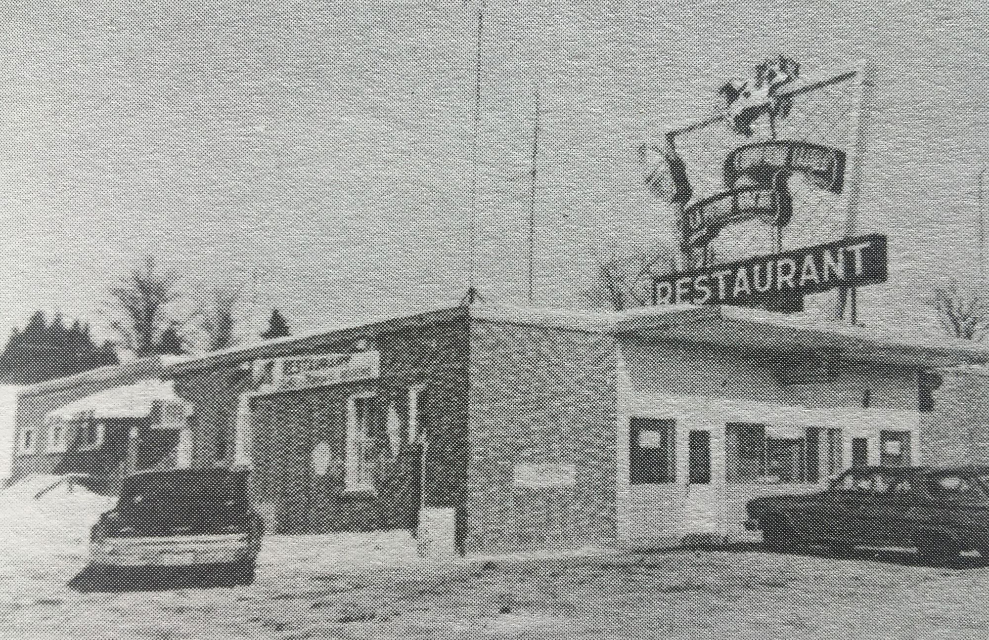 Black and white photo of a building with a badge reading “Restaurant” and two cars parked in front.