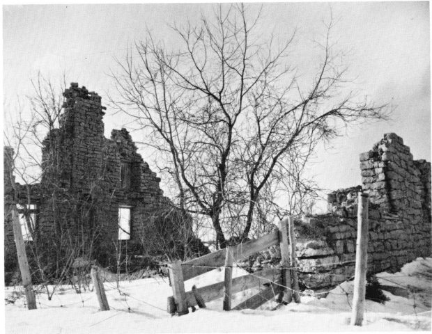 Black and white photo of the ruins of a house in winter.