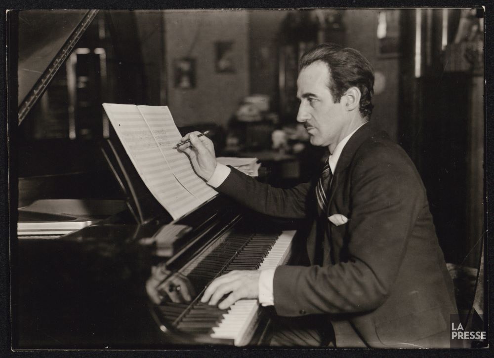 Black and white photo of Rodolphe Mathieu seated at the piano and composing.