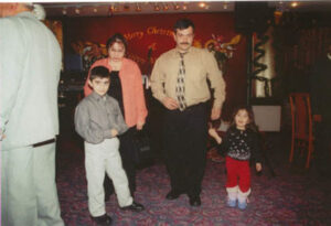 Analog photograph showing a two adults and two young children in a restaurant with a banner behind them reading 