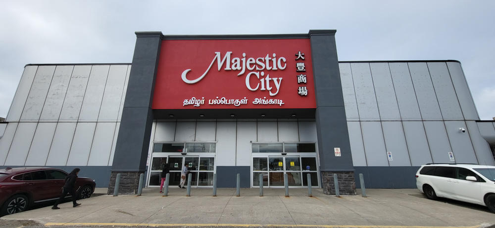 Front entrance of Majestic City Mall with large red signage displaying the mall's name in English and Asian characters, under a cloudy sky.