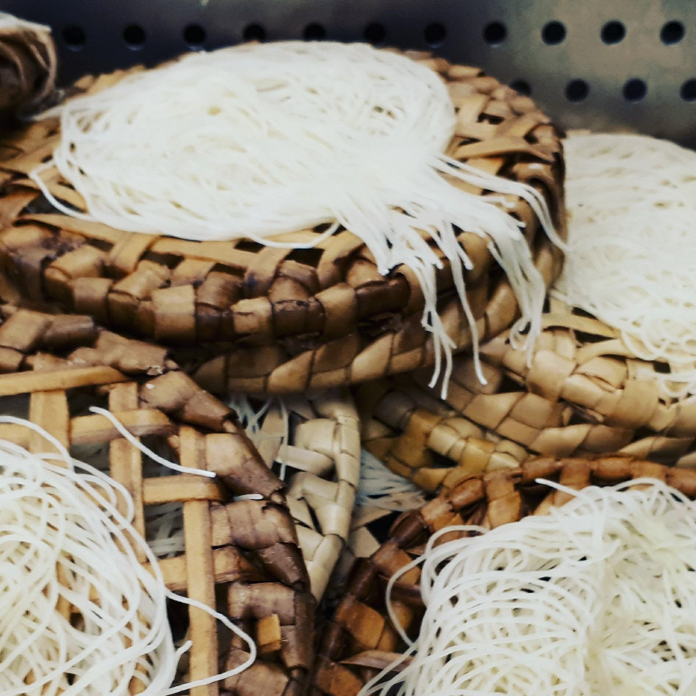 A close up of a woven bamboo wicker basket containing white, thin rice noodle nests.