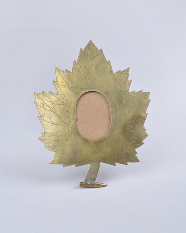 An engraved, maple leaf shaped frame with a circular hole for a picture.