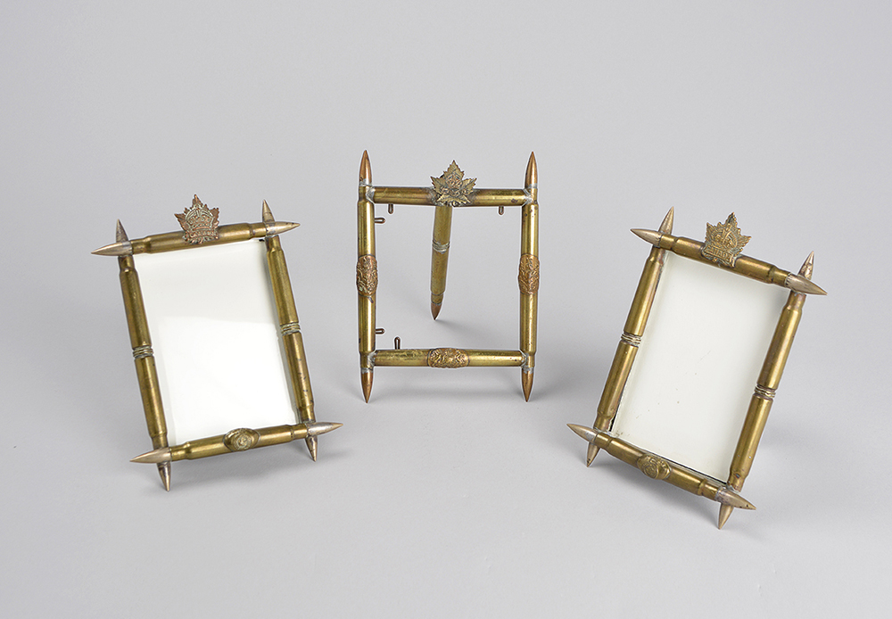 Three picture frames made from polished bullet casings. There are maple leaf medals on the frame.