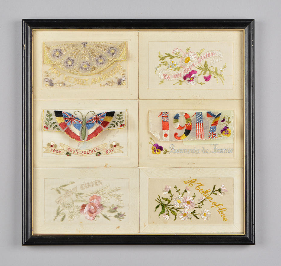 Six colourful embroidered silk postcards in a black wooden frame.