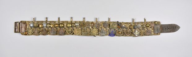 A very ornate belt made from a collection of brass medals and badges.