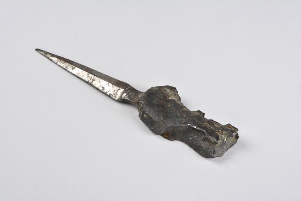 A dull-edged blade, acting as a letter opener, is attached to a handle made from a rough shell fragment handle.