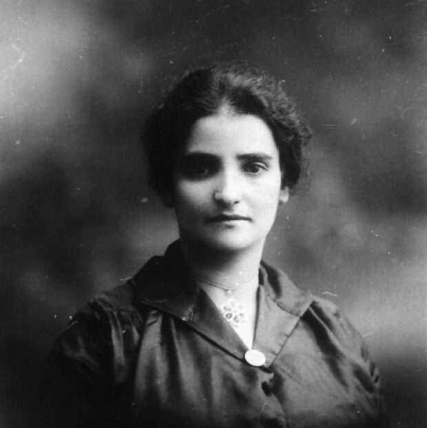 Black and white portrait of a woman with dark hair and dark eyes wearing dark clothes, and a flower necklace with her hair up.