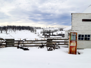 Winter scene of old farm equipment, gas pump and wooden building before wooded hill