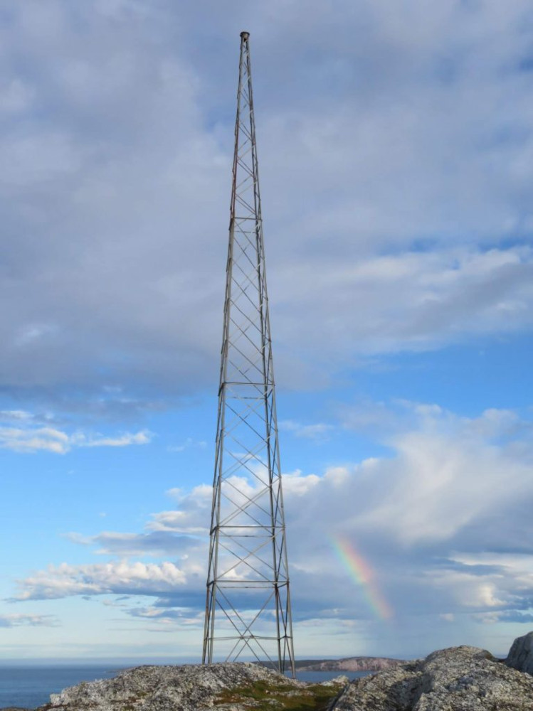A tall aerial tower on flat coastal rocks, with a rainbow.