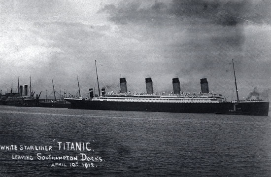 A large ship with four funnels steams to the right out of a port, leaving behind smaller vessels. Written on the photograph is: “White Star liner ‘Titanic.’ Leaving Southampton Docks, April 10th, 1912.”