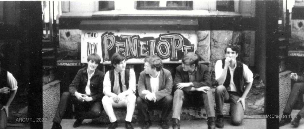 Black and white photograph of five young members of the group Sidetrack seated outdoors in front of a sign that reads The New Penelope. Portions of similar images can be seen on the far right and far left side from this strip of images taken from a film negative strip.