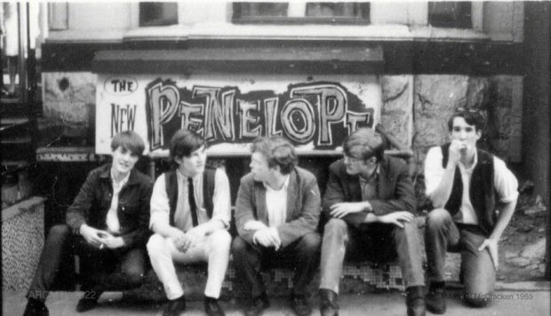 Black and white photograph of five young members of the group Sidetrack seated outdoors in front of a sign that reads The New Penelope.