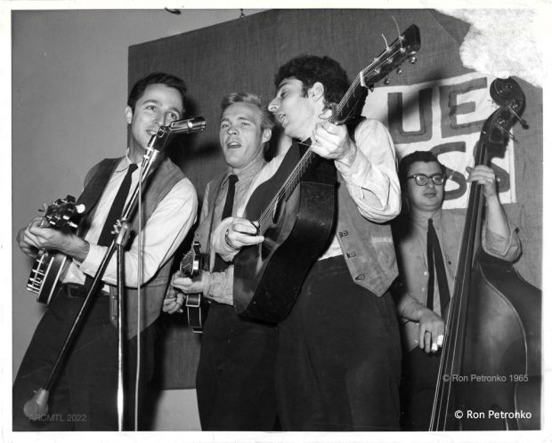 Black and white photograph of four men wearing vests and ties singing and playing guitars, mandolins and a standup bass.