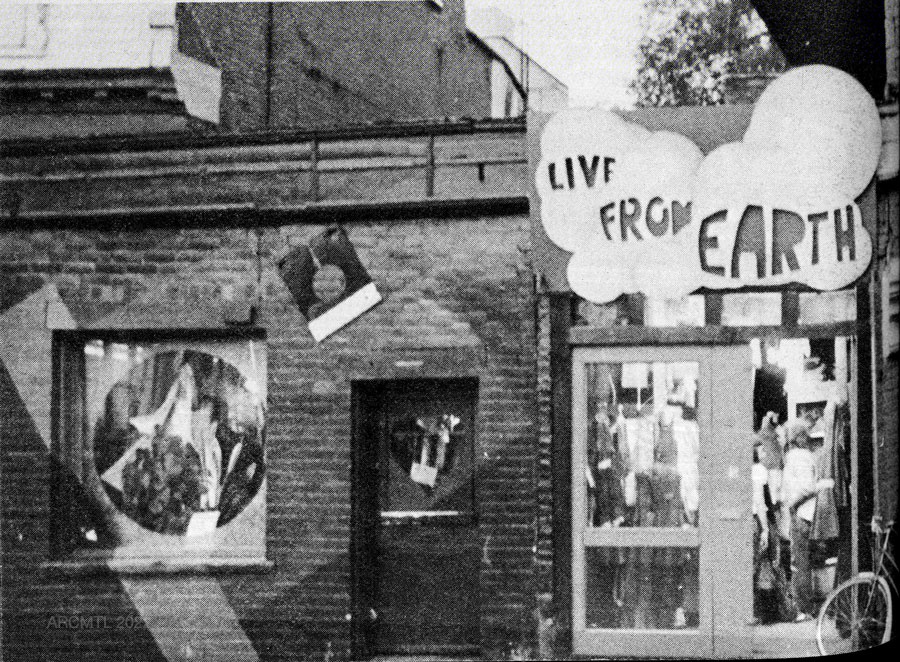 Black and white photograph of a storefront with a handmade sign with store name in rounded letters spelling Live from Earth.