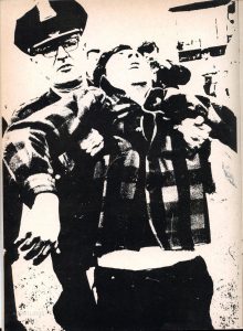 Black and white photo of a policeman holding by his underarms a distressed, limp young man wearing a checkered shirt.