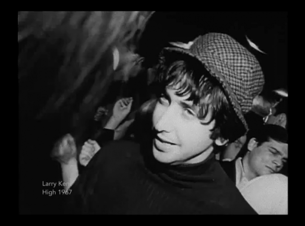 A still image taken from the film High showing a young man wearing a hat in the foreground of a group of young people dancing.