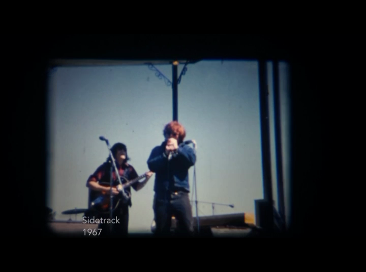 Two members of the musical group Sidetrack are seen in the centre of a screenshot from a video of their performance outdoors in a Montreal park.