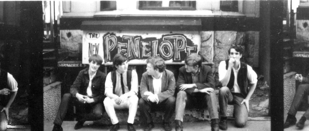 Black and white photograph of five young members of the group Sidetrack seated outdoors in front of a sign that reads The New Penelope. Portions of similar images can be seen on the far right and far left side from this strip of images taken from a film negative strip.