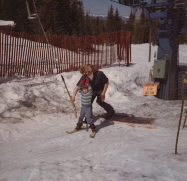 Colour photograph of ski lift attendant helping a small child grab onto the T-bar lift.