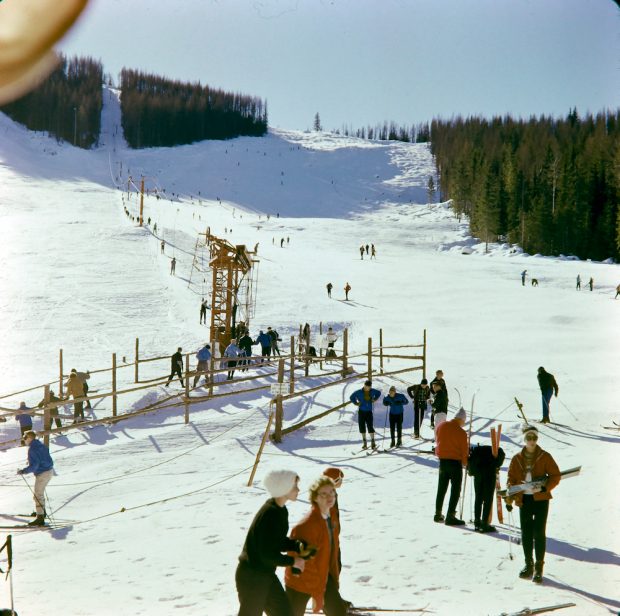 Colour photograph of skiers standing in line to use a ski lift.