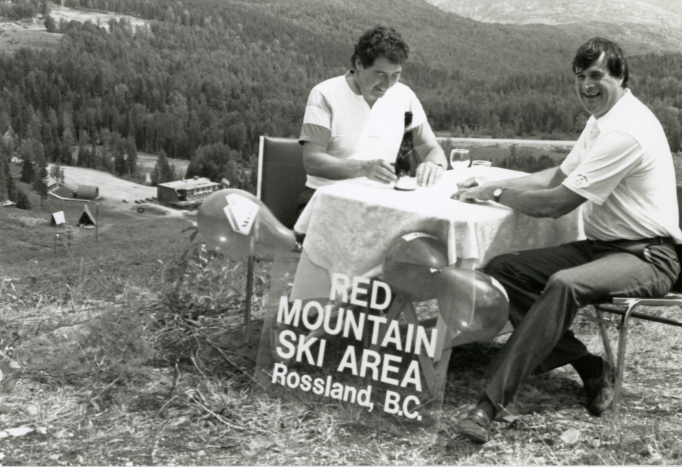 Two men sitting at a table on a mountain signing documents.