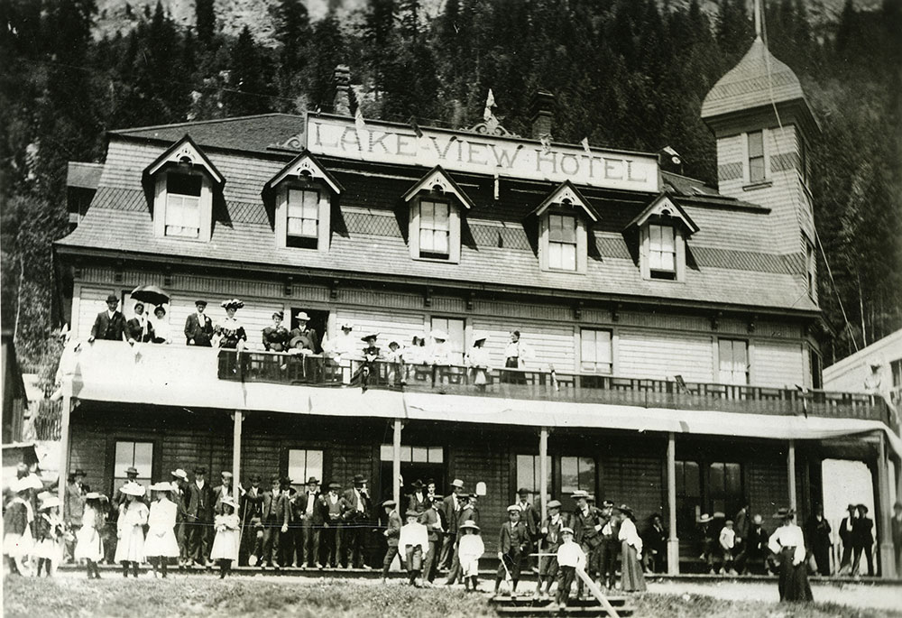 Black-and-white photograph of a two-storied hotel, with name "Lakeview Hotel" at the top. A crowd of people stand on and below the balcony. The people are in dress-attire - wearing suits, dresses, and hats.