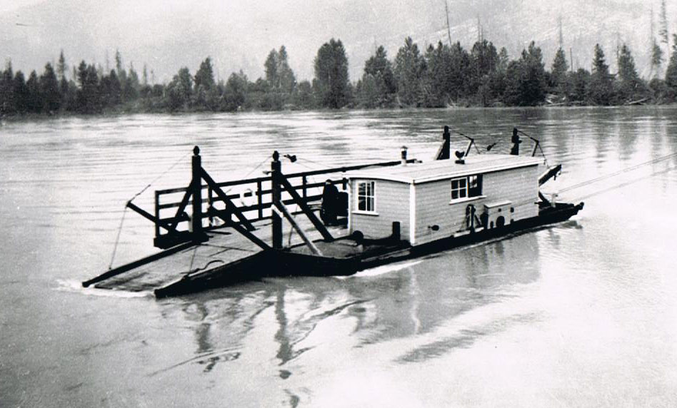 A black-and-white photograph of a ferry sitting on the open water. Trees in the background.