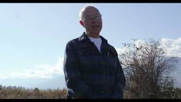 Bruce Tillen – a bald white man, wearing a white shirt and blue and black jacket. He is standing outside.