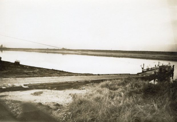 A sepia toned photograph of a ferry docked on the side of the water, with a ramp leading to the ferry.