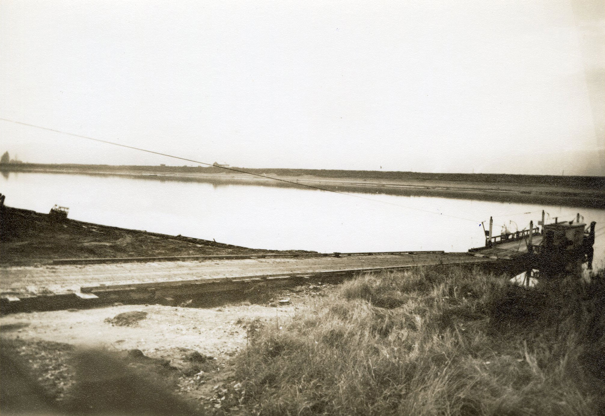 A sepia toned photograph of a ferry docked on the side of the water, with a ramp leading to the ferry.