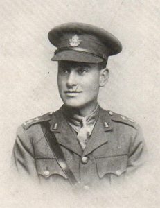 Portrait of a soldier wearing peak hat. Accoutrements and a belt can be seen on his shoulders and chest.