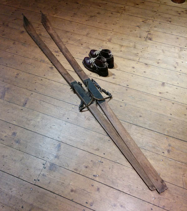 Wood skis with metal foot grip and leather attach. Ski boots are beside it.