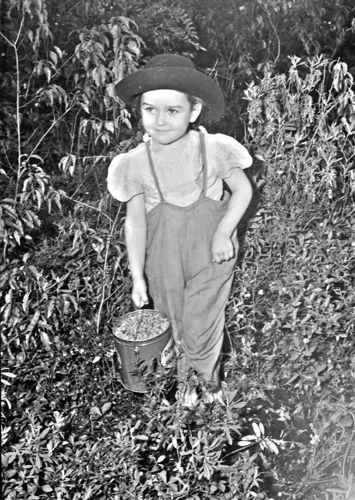 Black and white picture of a young girl in the woods with a basket filled with blueberries.
