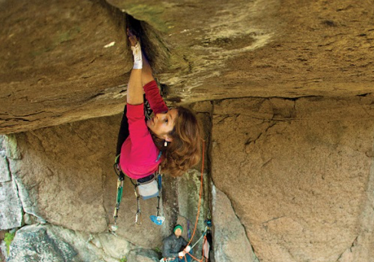 Close-up of a woman hanging on with hands and feet to the underside of an overhang with some 15 metres of reach
