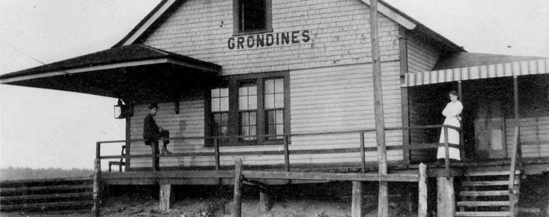 Black and white photo of a woman standing and a man sitting on the gallery of the Grondines train station.