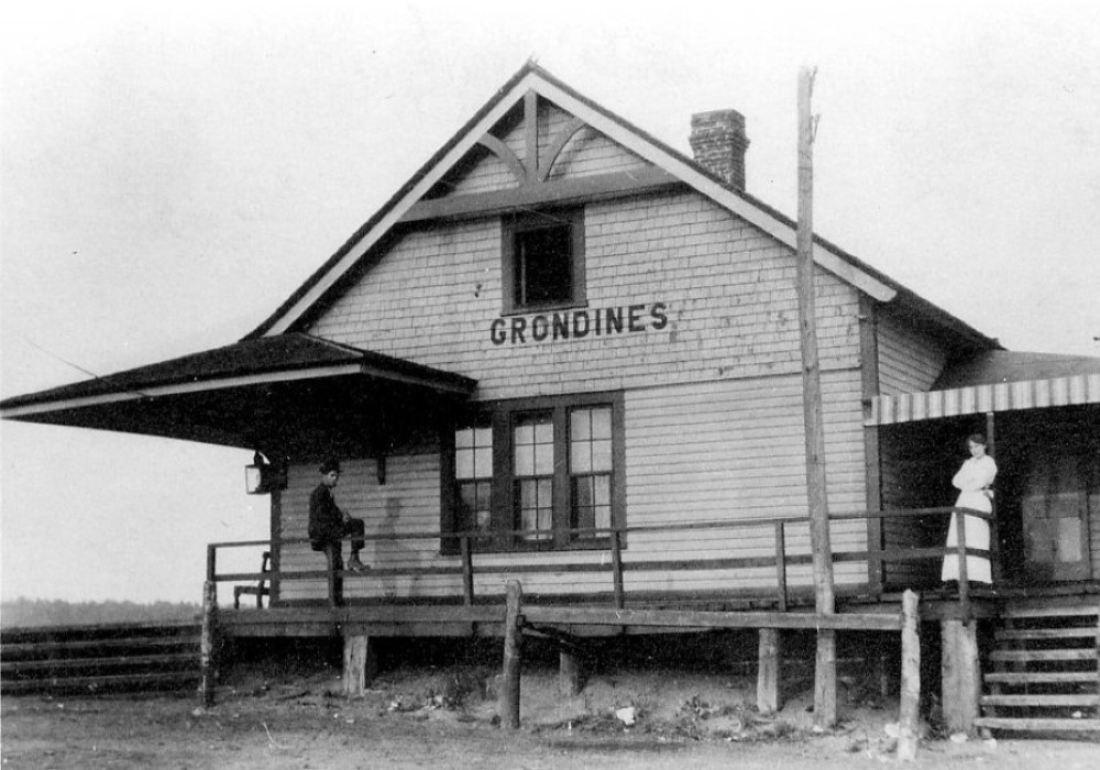 Black and white photo of a woman standing and a man sitting on the gallery of the Grondines train station.